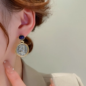 Detailed close-up of retro portrait coin earrings with blue gemstone on model ear