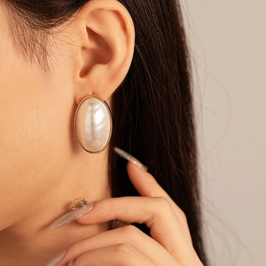 Close-up of a large oval pearl stud earring with a vintage gold frame on a model