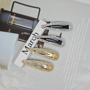 Close-up of four rhinestone metal hair clips in gold and silver on a white stone block