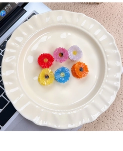 Detail of six colorful acetate daisy hair clips arranged on a white ceramic scalloped tray