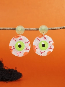 Detailed view of Halloween eyeball drop earrings hanging on a branch over orange background