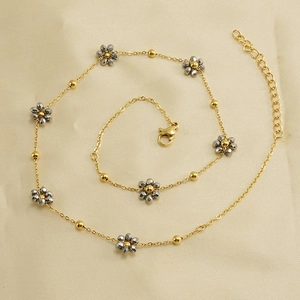 Golden stainless steel chain bracelet with gray faceted bead flowers on beige fabric