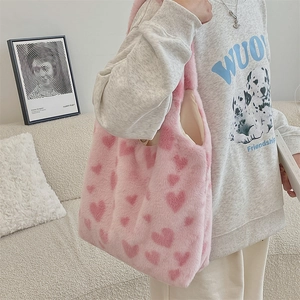 Detailed view of pink plush heart tote bag styled with a casual sweater in a home setting