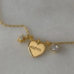 Gold MOM heart pendant necklace with round and oval zircon charms on marble background
