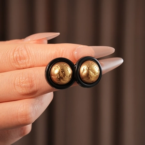 Close-up of matte black round earrings with textured golden sphere center detail