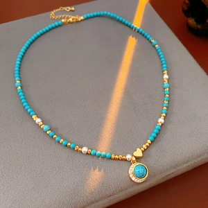 Détail du collier avec pendentif coeur turquoise et perles dorées sur support velours