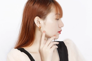 Detailed view of a gold flower earring with pink enamel petals on a model's ear