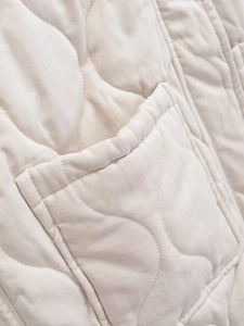 Detailed close-up of the beige quilted vest pocket and high-quality fabric texture