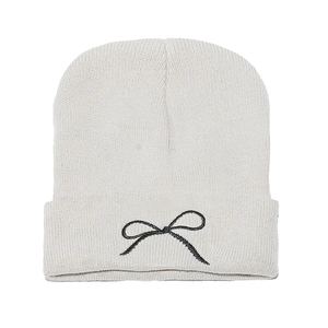 Close-up of white knit beanie featuring detailed black embroidered bow and ribbed cuff