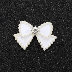 Detailed view of pearl bow charm with central rhinestone on a black glitter surface