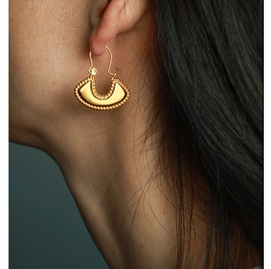 Macro shot of gold-plated D-shaped hoop earrings with intricate beaded edges on model