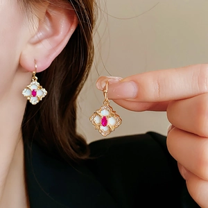Detail of gold floral clover earrings with red gemstone and white mother of pearl