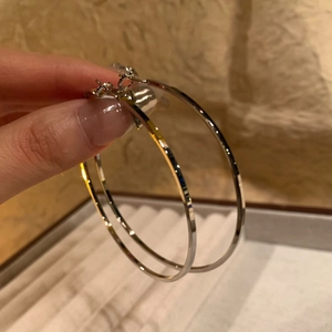 Detailed close-up of large silver hoop earrings held by hand to show size and mirror finish