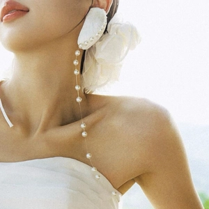 Macro detail of long silver needle earrings with shell petals and pearl tassels