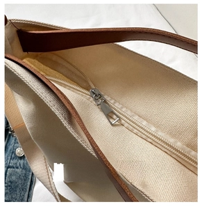 Close-up of smooth metal zipper on off-white canvas tote bag with brown leather handle