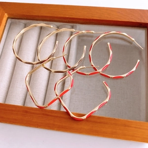 Detailed close-up of golden wavy hoop earrings with red enamel stripes on grey velvet