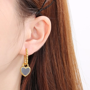 Gros plan de boucles d'oreilles dorées avec pendentif cœur en émail noir sur modèle