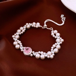Detail of double-strand pearl bracelet with pink gemstone pendant on brown silk fabric