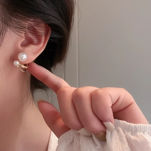 Close-up of golden C-shaped double hoop earrings with white pearls on a female model