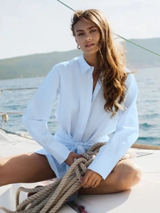 Close-up of light blue shirt dress with waist tie detail against a coastal background