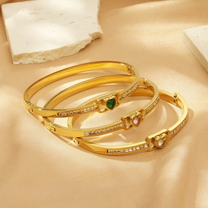 Macro detail of three gold heart bangles with emerald, pink, and clear zircon stones