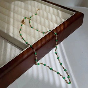 Detail of 18k gold plated titanium chain with green enamel beads on a wooden tray