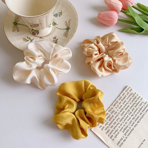 Elegant satin silk scrunchies in cream and champagne yellow set against a floral teacup background