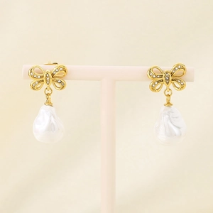 Close-up of golden bow earrings with baroque pearls and zircon inlay on pink stand