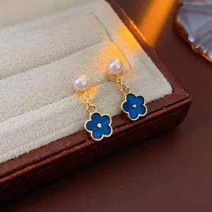 Close-up of gold flower earrings with white pearl and blue clover pendant on jewelry box