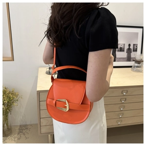 Detail of orange crescent crossbody bag featuring a striking gold metal clasp and leather texture