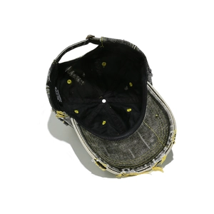 Détail d'une casquette en denim noir vieilli avec coutures jaunes et bords effilochés