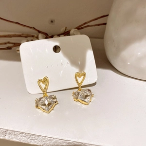 Detalle de pendientes de corazón bañados en oro con circón sobre tarjeta soporte