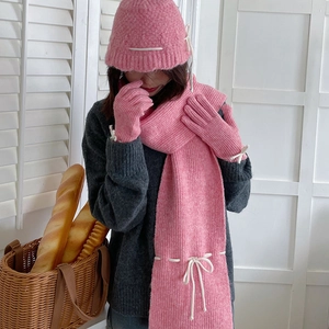 Close-up of pink knit scarf and hat set with delicate white bow tie details