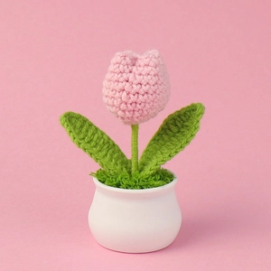 Close-up of handmade crochet pink tulip in a white ceramic pot with green leaves