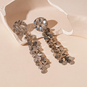 Detailed view of silver metallic sequin tassel earrings on a minimalist cream background