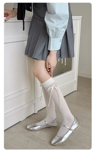 Close-up of white calf socks with delicate ribbon bows paired with silver Mary Janes