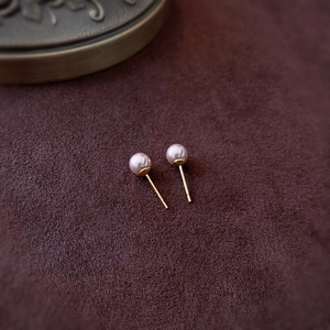Close-up of pink-purple pearl earrings with golden pins on a vintage brown suede background