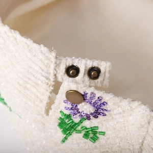 Detail of cream corduroy hat featuring purple sequin flowers and green beaded stems