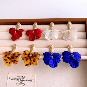 Flat lay of four pairs of colorful acrylic petal pendant earrings on a beige velvet tray