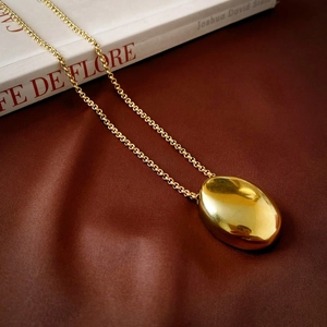 Macro detail of polished gold oval pendant on a delicate chain against silk fabric