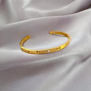 Detailed close-up of golden stainless steel Roman numeral bangle with a single zircon stone