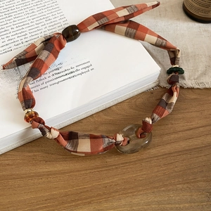 Detail of a vintage orange plaid fabric necklace with resin beads on an open book