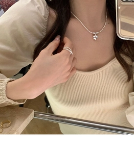 Close-up of elegant silver heart necklace and cross ring worn by a female model