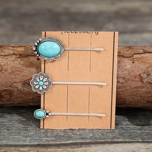 Three vintage turquoise alloy flower hair clips on card over a rustic wood background