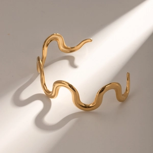 Irregular wavy stainless steel bangle for women plated in 18k gold on a white surface