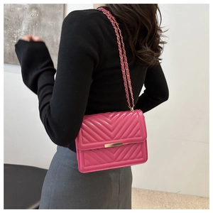 Detail der rosa gesteppten Umhängetasche mit V-Muster und goldener Kette an einem Model