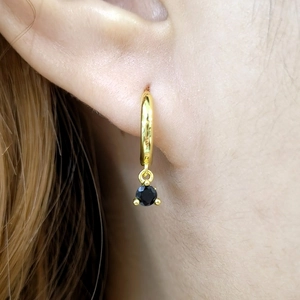 Macro shot of gold hoop earrings with black faceted gemstone pendant worn on ear