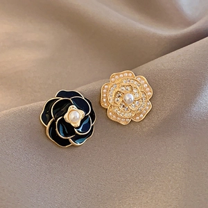 Macro shot of camellia stud earrings with enamel, pearls, and gold finish on silk