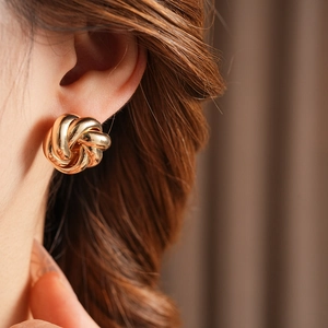 Close-up of elegant gold twisted knot stud earring worn by model in warm natural light