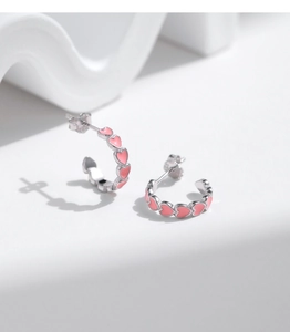 Macro detail of s925 silver heart stud earrings with pink enamel on a wavy background